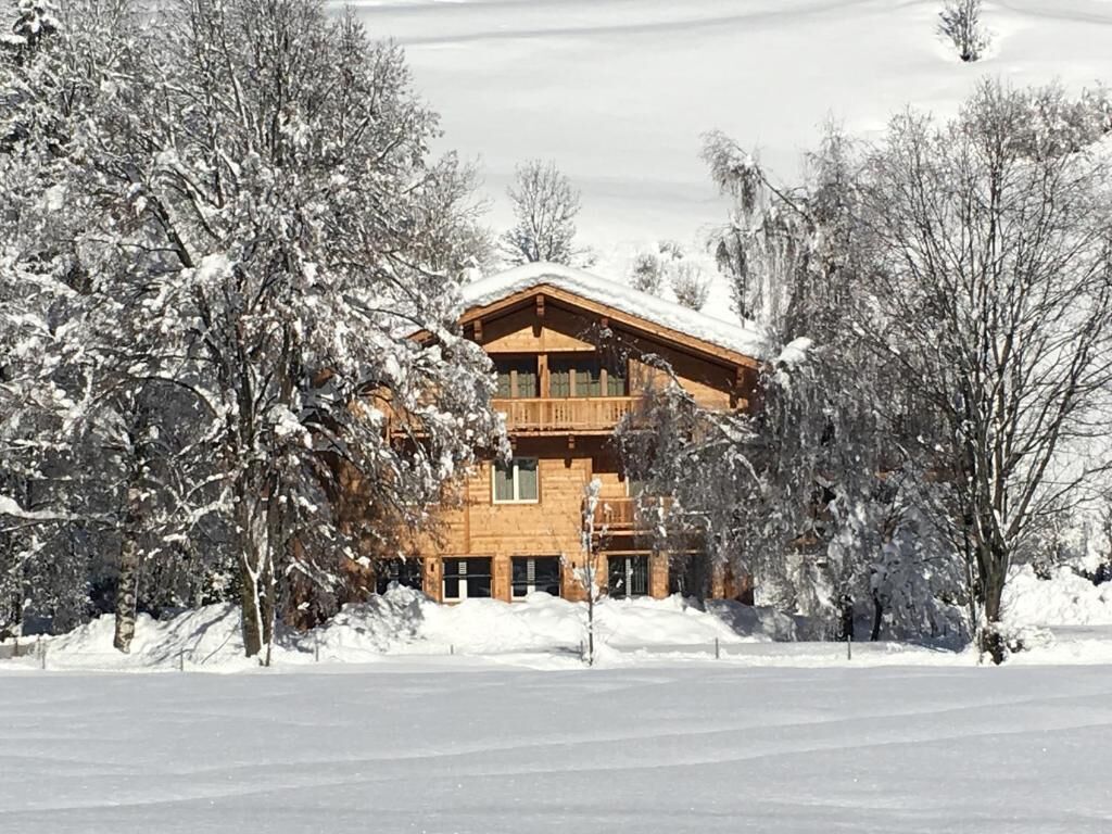 Un chalet en bois doté d’un balcon, entouré d’arbres couverts de neige.