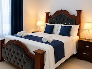 A neatly made bed with a dark headboard and white bedding, two bedside tables with lamps, and a window with curtains. - Modern Cozy apartment (Boca Chica)