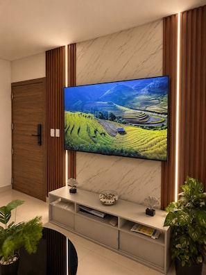 A flat-screen TV mounted on a wall with a marble finish, flanked by wooden panels, and a white entertainment unit below. - Modern Cozy apartment (Boca Chica)