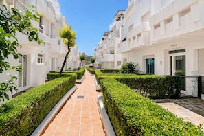 A pathway flanked by neatly trimmed hedges and white buildings with balconies and windows. - Vr1b - Golfside Escape Near Estepona (Estepona)