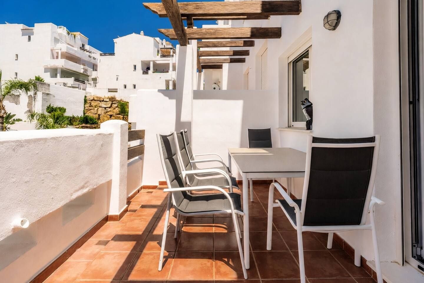 A balcony with a table and chairs, white walls, and a view of white buildings.
