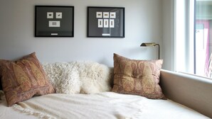 Una cama con una manta blanca y almohadas estampadas, un cuadro en la pared y una ventana con vistas.