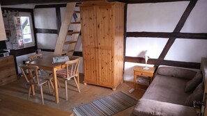 Ein Zimmer mit Holztisch, Stühlen, einem Schrank, einer Leiter, einem Sofa und einem Fenster.