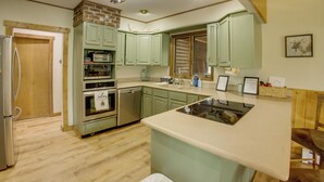 Una cocina con gabinetes verdes, un refrigerador, un horno, un lavavajillas y piso de madera.