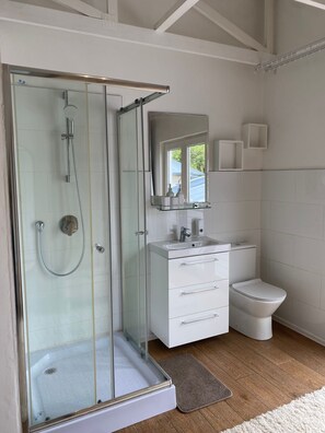 Ein modernes Badezimmer mit einer gläsernen Duschkabine, einem weißen Waschtisch mit Schubladen, einer Toilette und einem Spiegel über dem Waschbecken.