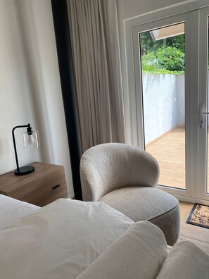 Ein Hotelzimmer mit einem Bett, einem Sessel, einem Nachttisch mit Lampe und einer Glasschiebetür, die zu einem Außenbereich führt.