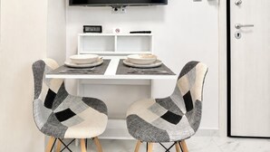 A dining area with a TV mounted on the wall, a digital clock, and a door with a lock. - Athens Explorer Studio Near Transit by ΜΡS (Agios Ioannis Rentis)