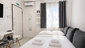 A hotel room with a bed, a desk, a chair, a mirror, a shelf with toiletries, and a window with curtains. - Athens Explorer Studio Near Transit by ΜΡS (Agios Ioannis Rentis)