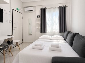 Une chambre d’hôtel comprenant un lit, un bureau, une chaise, un miroir, une étagère avec des articles de toilette et une fenêtre avec des rideaux.