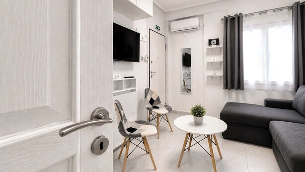 A modern living room with a sofa, a small round table with a plant, and a TV mounted on the wall. - Athens Explorer Studio Near Transit by ΜΡS (Agios Ioannis Rentis)