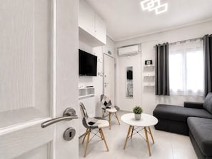 A modern living room with a sofa, a small round table with a plant, and a TV mounted on the wall.