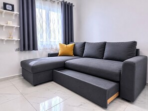 Un salon moderne avec un canapé d’angle, une petite table et une fenêtre avec des rideaux.