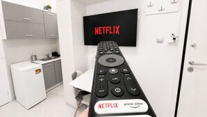 A modern kitchen with a washing machine, a TV mounted on the wall displaying 'NETFLIX', and a remote control with buttons for Netflix, Prime Video, YouTube, and TCL CHANNEL. - Athens Explorer Studio Near Transit by ΜΡS (Agios Ioannis Rentis)