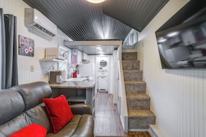 Un espacio habitable compacto con kitchenette, una escalera y un sofá de cuero con cojines rojos.