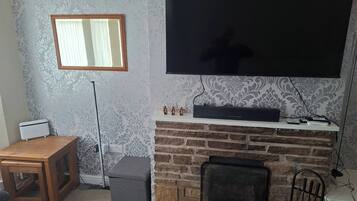 Ein Wohnzimmer mit an der Wand montiertem Fernseher, Kamin, einer Holzbank und einem kleinen Tisch.