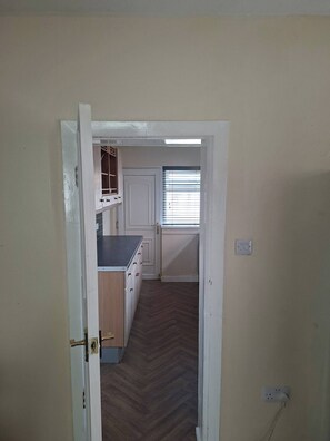 Un pasillo que conduce a una cocina con armarios de madera, una encimera y una ventana con persianas.