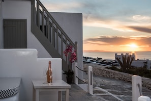 A terrace with a table, a bottle, and a glass, overlooking a sunset and a marina.