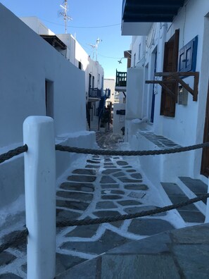 Um caminho de pedra estreito ladeado por edifícios brancos com varandas e portas de madeira.