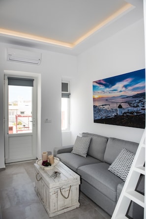A modern living room with a grey sofa, a white coffee table with decorative items, a wall-mounted air conditioner, and a large landscape painting.