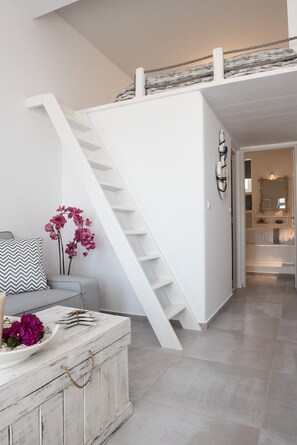 Uma escada leva a um quarto no mezanino, com uma cama, mesa de cabeceira e cômoda.