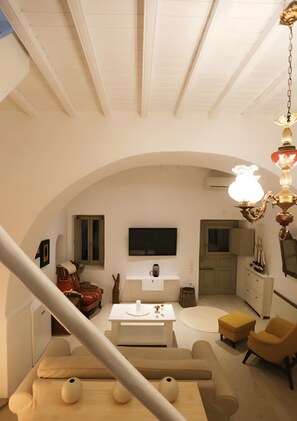 A spacious living area with a high ceiling, a television mounted on the wall, a sofa, a coffee table, and a chandelier. - Christy’s Three-Level Villa in Mykonos Town (Mykonos)