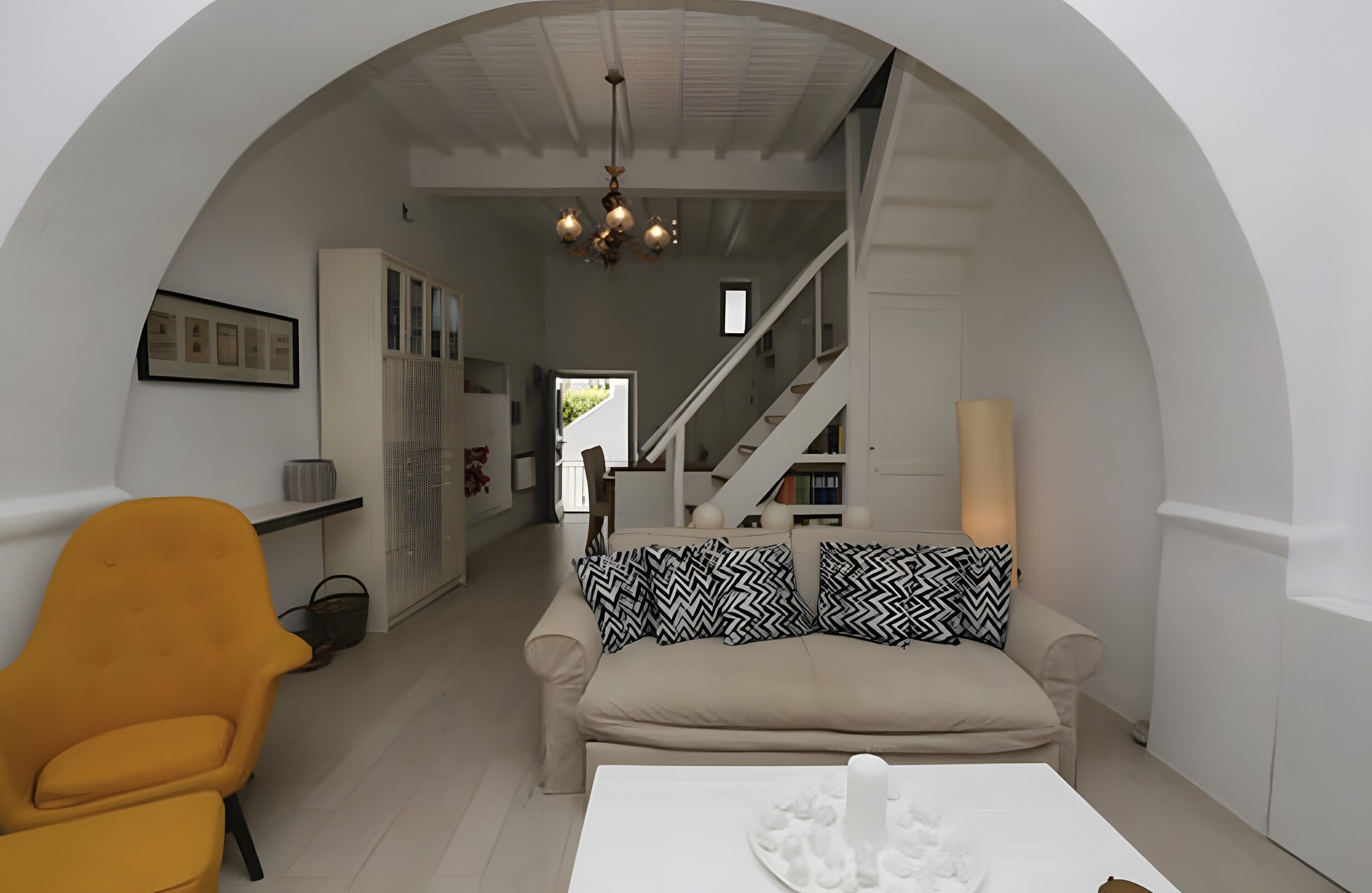 A modern interior with a sofa, a yellow chair, a staircase, and a chandelier.