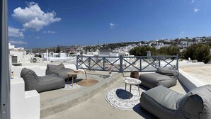 En tagterrasse med udendørs siddepladser og udsigt over en kystby, under en klar himmel.