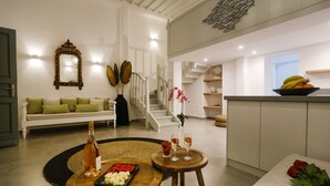 En moderne stue med sofa, spisebord med mad, en flaske vin og en trappe op til et køkken.