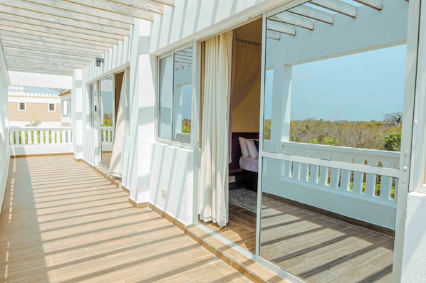 Un pasillo con suelo de madera, paredes blancas y puertas de cristal que dan a una habitación con cama y vistas al paisaje.