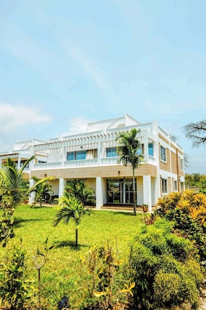 A modern building with a flat roof, large windows, and a well-maintained lawn with various plants.
