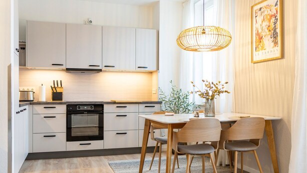 A modern kitchen with white cabinets, a built-in oven, and a dining area with a table and chairs. - Vacation apartment M6 - "Kommodig Oorloff" - 3-room apartment close to the beach for 4 people (Graal-Müritz)