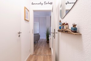Ein Flur mit einer Tür zu einem Zimmer, einem Spiegel und einem Regal mit Kleinigkeiten.