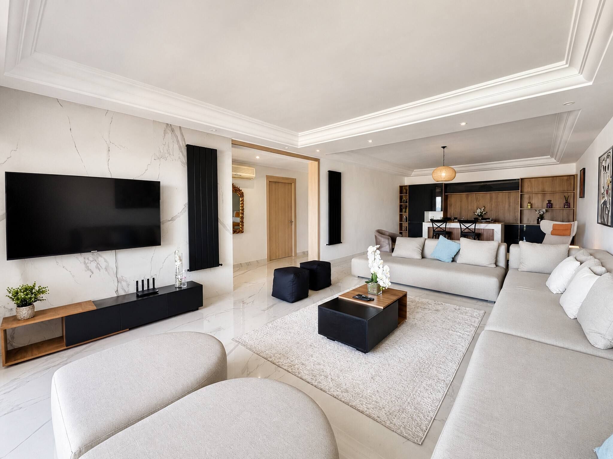 Un salon moderne avec un téléviseur à écran plat, un ensemble de canapés, une table basse et un coin cuisine à l’arrière-plan.