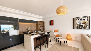 Une cuisine moderne avec un îlot central, un coin repas avec des chaises, un canapé et un grand tableau abstrait accroché au mur.