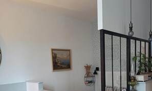 A room with a painting, a potted plant, a lamp, and a staircase with a black railing. - Very pretty studio 100 meters from the main beach and pedestrian streets. (Les Sables-d'Olonne)