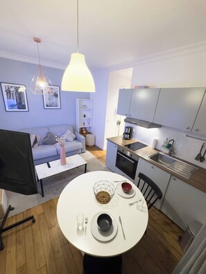 A compact living space with a dining table, kitchen area, and a sofa. - Charming Studio in the Heart of Paris' 18th Arrondissement (Paris)