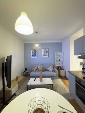 Ein modernes Wohnzimmer mit Sofa, Couchtisch, Fernseher und Küchenzeile mit Schränken und Arbeitsplatte.