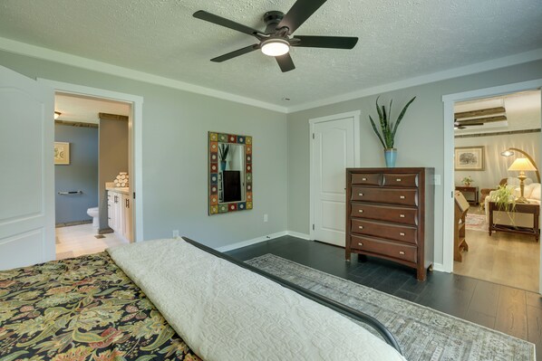 A bedroom with a bed, a dresser, a ceiling fan, a mirror, and a door leading to another room.