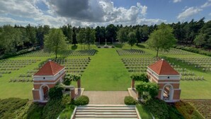 Un cimetière avec des rangées de tombes, deux petits bâtiments en briques et un ciel dégagé.