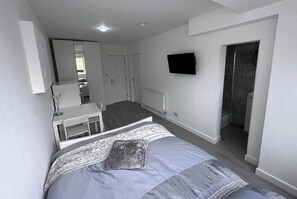 A bedroom with a bed, a desk, a television, and a shower.
