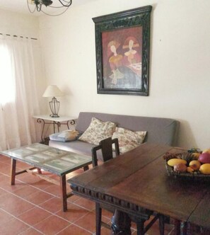 A living room with a sofa, a coffee table, a dining table, a framed artwork, and a fruit basket. - Modern Holiday Rental for Two Guests (Membrio, Cáceres)