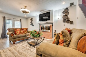 Una sala de estar con sofá, mesa de centro, chimenea y televisor montado en la pared.