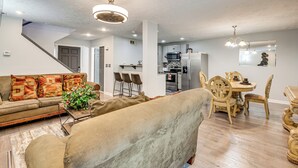 A living room with a sofa, a dining table with chairs, a kitchen area with appliances, and a staircase. - 3BR Townhome Near Downtown Decatur (Decatur)