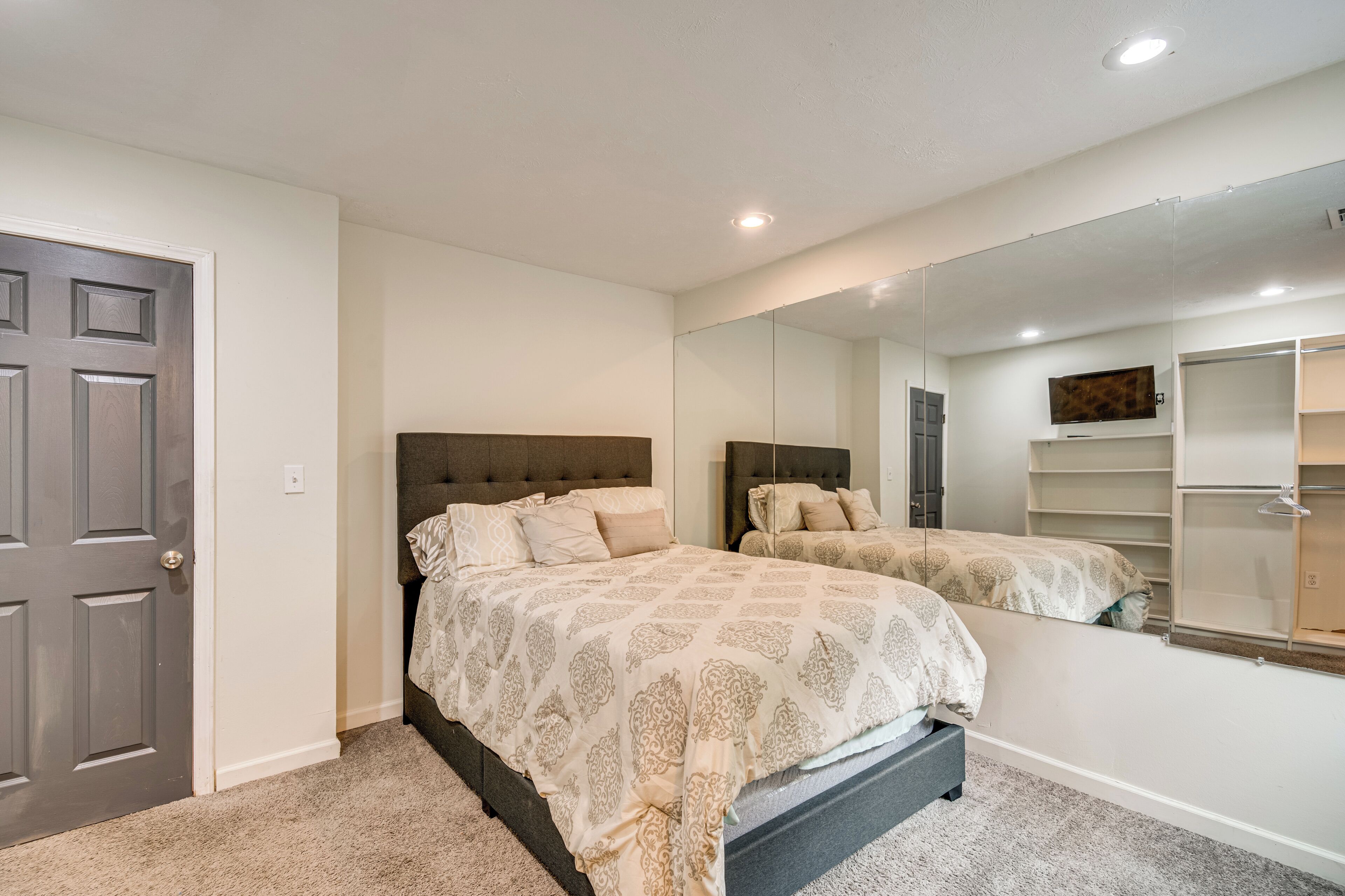 Un dormitorio con cama, un espejo grande, un armario y una puerta.