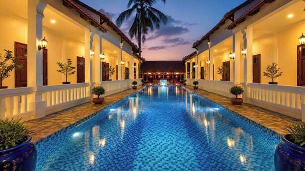 A swimming pool with a tiled floor, flanked by two-story buildings with balconies and potted plants. - Sunset Cove Boutique Resort (Phu Quoc)