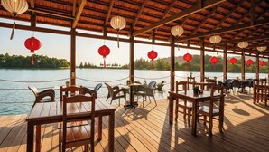 An outdoor dining area with wooden tables and chairs, red lanterns, and a view of a lake. - Sunset Cove Boutique Resort (Phu Quoc)