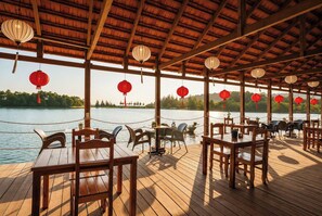 An outdoor dining area with wooden tables and chairs, red lanterns, and a view of a lake. - Sunset Cove Boutique Resort (Phu Quoc)