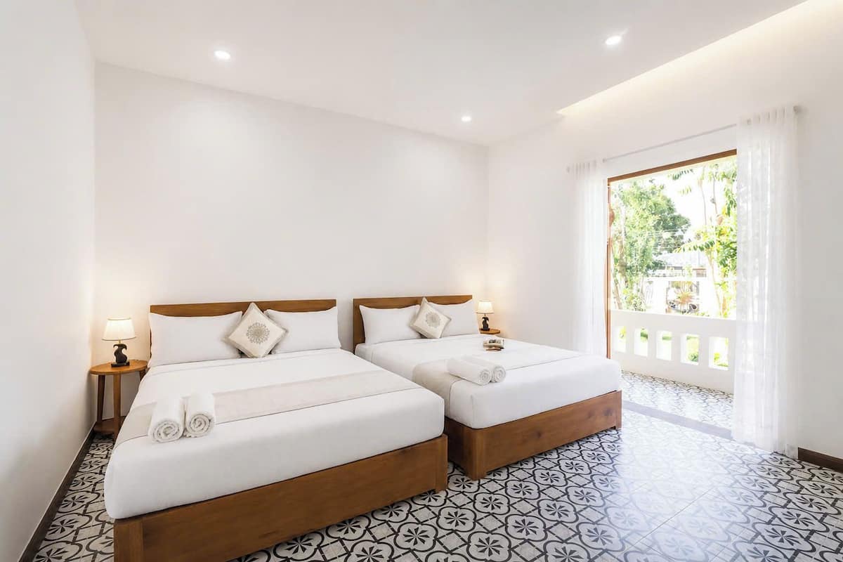 A hotel room with two beds, a large window with curtains, and patterned floor tiles.