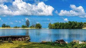 A calm lake with a wooden dock, surrounded by dense trees and a clear blue sky. - Sunset Cove Boutique Resort (Phu Quoc)