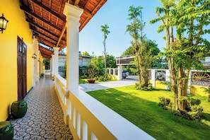 A covered outdoor area with a tiled floor, a yellow wall, and a view of a well-maintained lawn and trees.